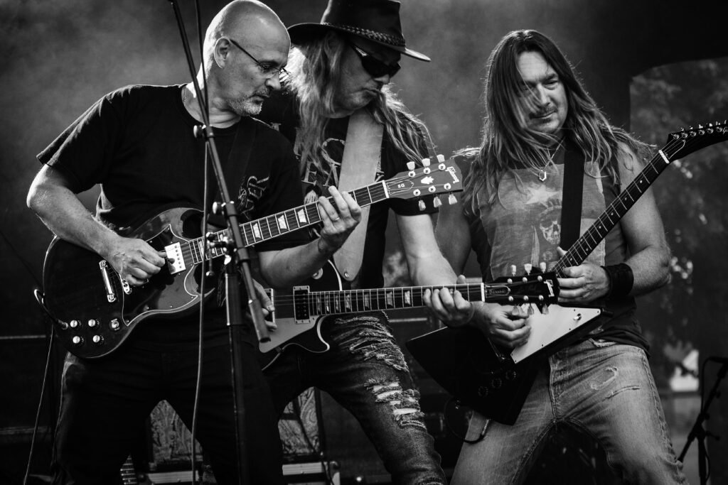 Black and white image of a rock band passionately performing on stage with guitars.
