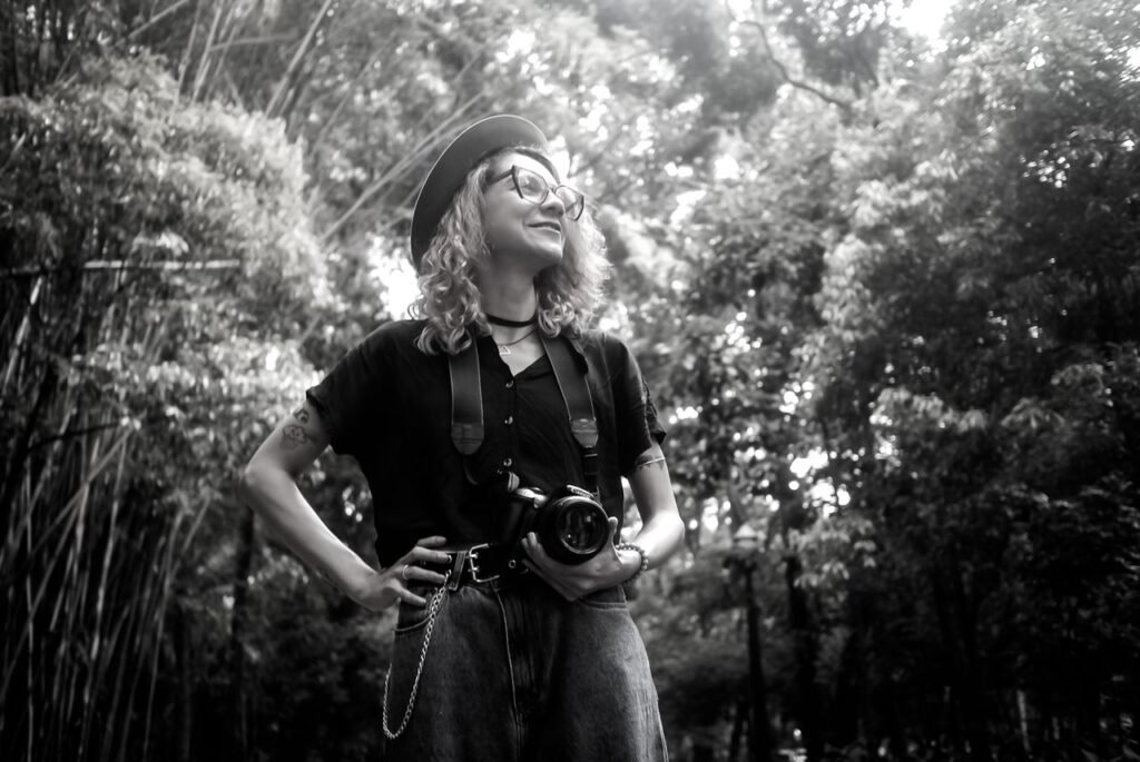 Black and white portrait of a confident photographer with her camera in a lush outdoor setting.